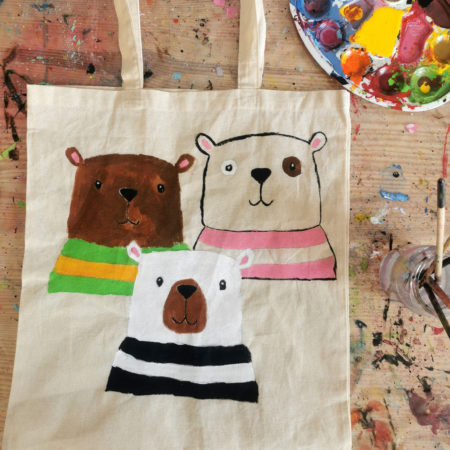 bawełniana torba z namalowanymi 3 misiami, obok torby lezy paleta z kolorowymi farbami